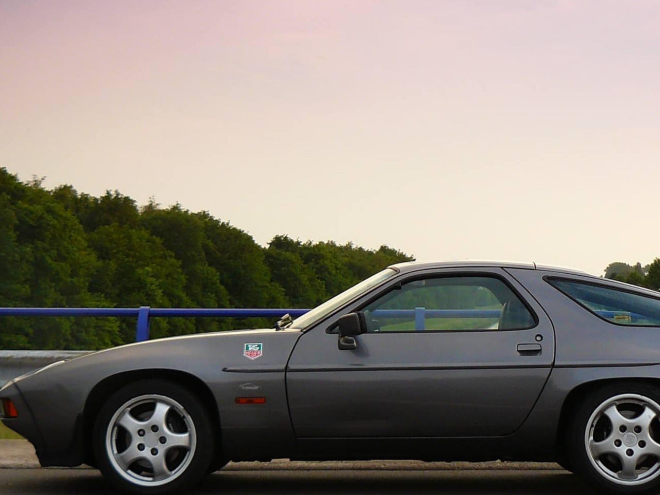 Gray sports car on a road with trees and a sunset in the background